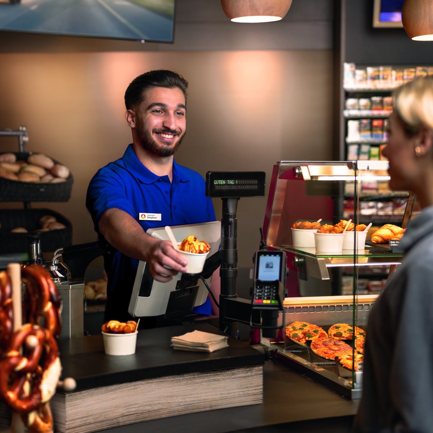 A bakery employee serves a cup of pretzel bites to a customer.