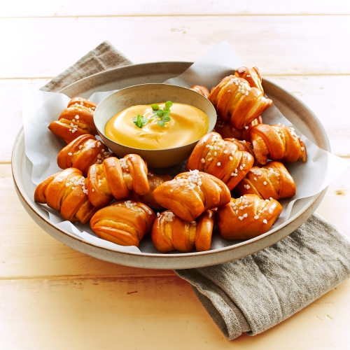 Rustic plate with Pretzel Bites and cheese dipping sauce in a small metal bowl.