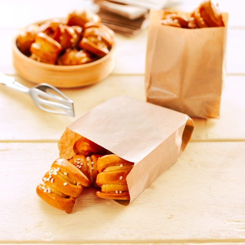 Brown and white paper bags with overflowing Pretzel Bites on a light wooden surface.