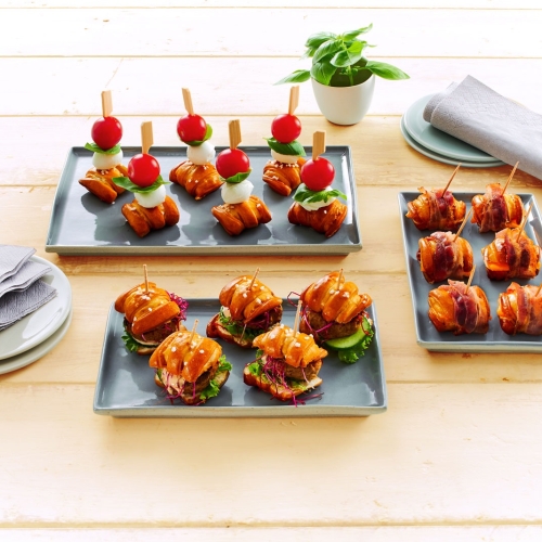 Drei Tabletts mit Pretzel-Bite-Fingerfood: Caprese, Speck-Bites und Mini-Burger-Slider.