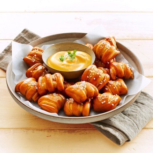 Rustikaler Teller mit Ditsch Pretzel Bites und goldgelber Kaese-Dipsauce in der Mitte.