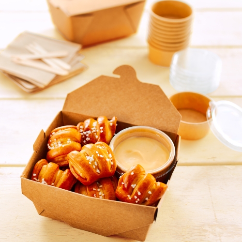 Take-away-Box mit Pretzel Bites und Sauce-Schale auf hellem Holzuntergrund.