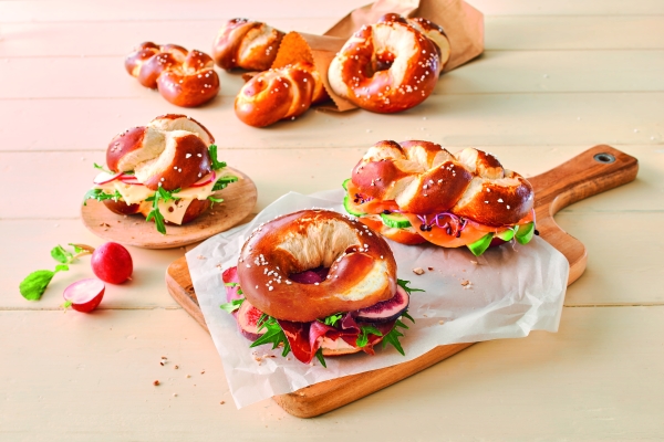Three Ditsch lye pretzels as sandwiches with radishes, lettuce and cheese on a wooden board.