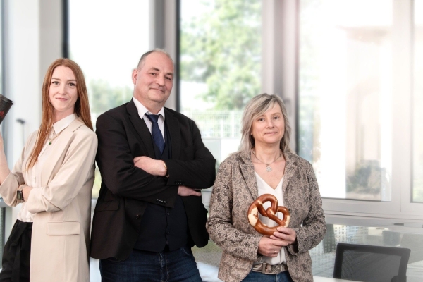 Three Ditsch employees standing in a bright office, holding a branded coffee cup and a pretzel.