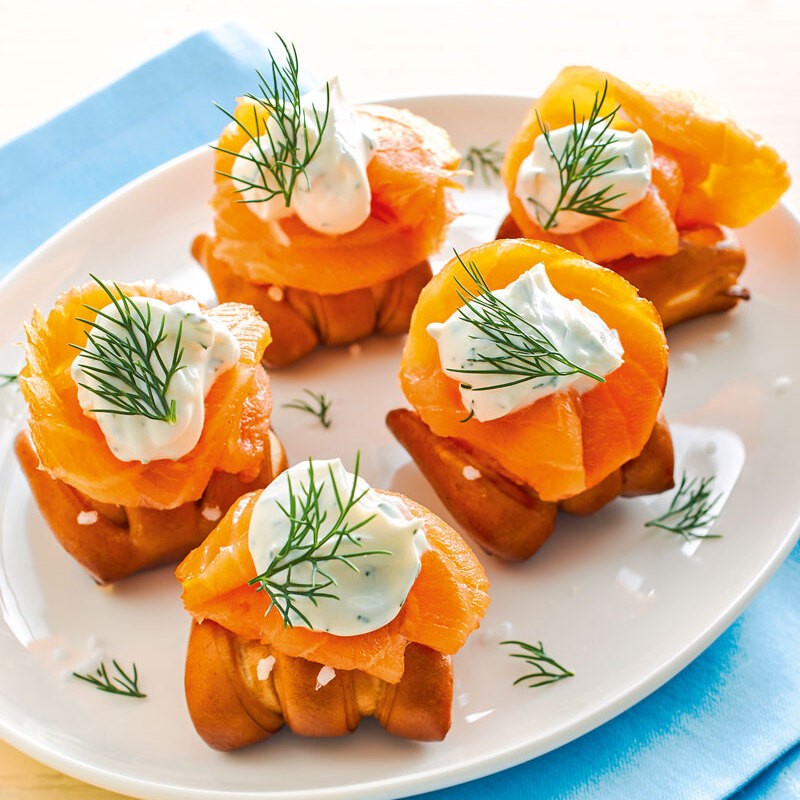 Five Pretzel Bites with smoked salmon, cream cheese and dill on a white plate.