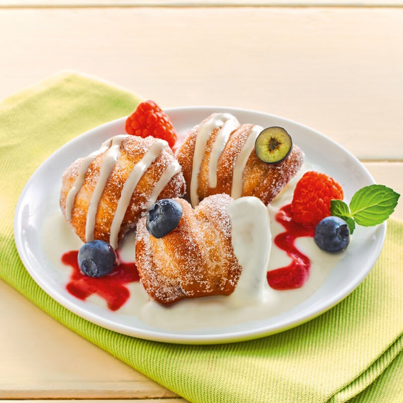 Drei zuckerbestreute Dessert Bites mit Beeren, Coulis und Sahne auf weissem Teller.