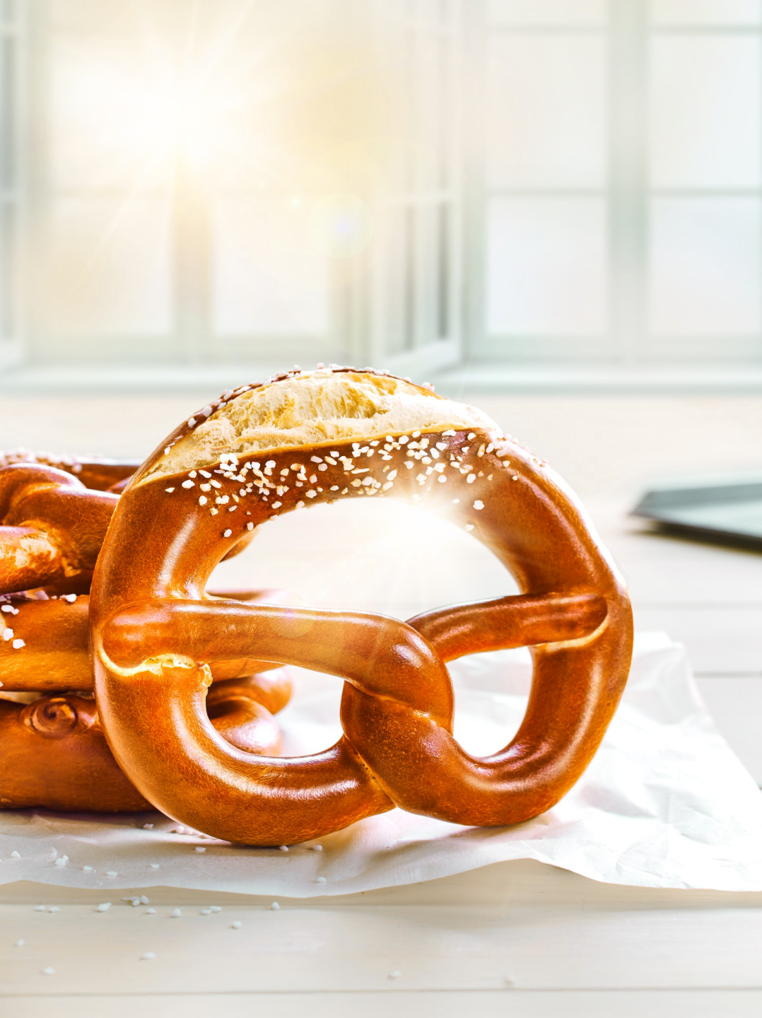 Einzelne braun gebackene Brezeln angelehnt an weitere Brezeln. Im Hintergrund strahlende Sonne.