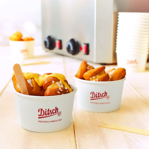 Goldbraune Ditsch Pretzel Bites in einem weisen Becher mit Ditsch-Aufschrift. Bites haben ein Saucen Topping.