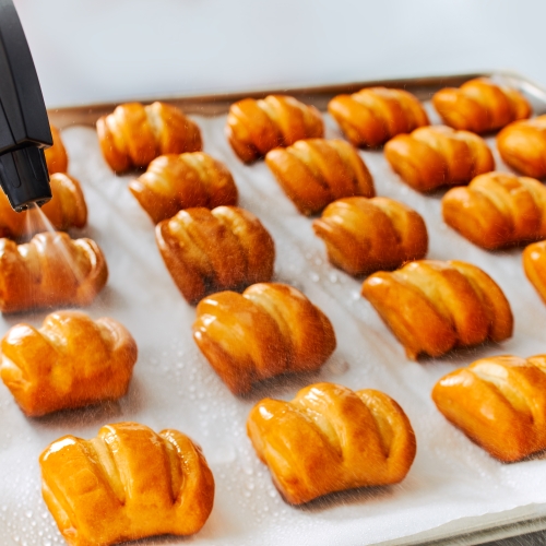 Pretzel Bites auf Backblech, Wasser wird aus Pumpbehaelter gesprüht..